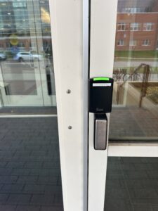The automatic door opener for the set of doors is located to the right of the set of doors door and is a silver/grey rectangular button with completely faded wording. The button is located directly under the Pcard reader. 