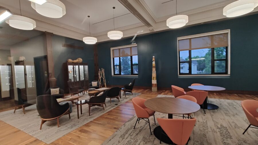View of the southern half of the Faculty/Staff Lounge, showing 2 exterior windows, seating area with low tables, and seating area with desk-height round tables.